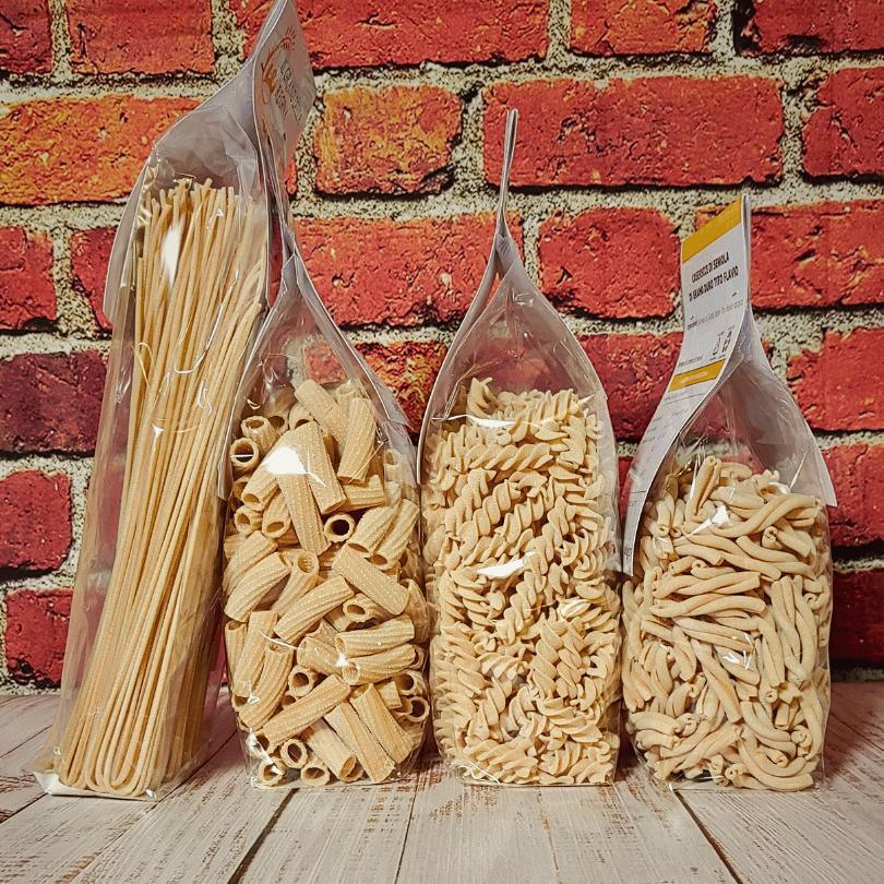 Quattro tipi di pasta all'uovo artigianale in confezioni trasparenti su tavolo di legno, sfondo muro in mattoni, C'era una volta - Bottega delle Mucche - Trecate (NO)